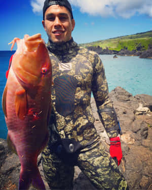 穿著潛水衣的男人在岩石海灘上拿著大粉紅魚