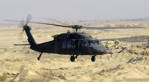黑色軍用直升機低空飛越沙漠建築工地。