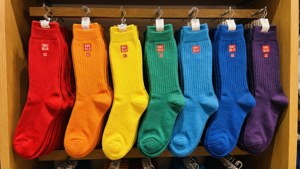 七雙彩虹色的 Uniqlo 船襪掛在商店的木製展示掛鉤上。