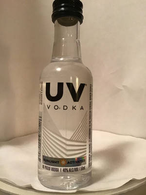 一個細細嘅透明伏特加酒樽，黑色樽蓋同幾何標籤，喺白色紙巾上面。