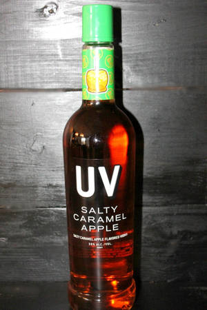 木質表面上的UV Salty Caramel Apple伏特加酒瓶。 — 紅色 壁紙