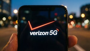 手拿著手機，在夜間顯示 Verizon 5G 標誌，背景有城市燈光