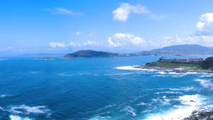 陽光明媚的天空下，海浪拍打和遠山構成的海岸景色。
