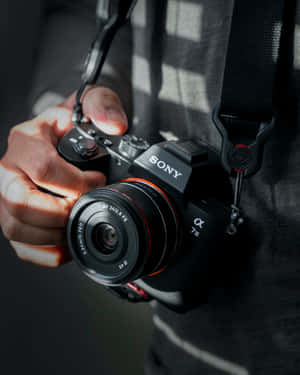 特寫一隻手拿著帶紅色鏡頭環的Sony Alpha 7 III相機。