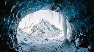 通過一個帶有冰柱的天然冰拱門看到的積雪山頂。