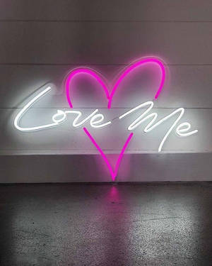 粉紅色心形和白色「Love Me」霓虹燈牌在木牆上發光，地板有倒影。