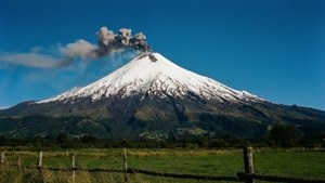 積雪火山在綠色田野上噴煙，有木柵欄