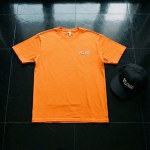 橙色Vlone T恤和帶有白色標誌的黑色帽子在黑色瓷磚地板上。 — Tecno Phantom V Flip 壁紙