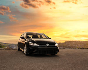黑色Volkswagen Golf R在日落時停在道路上，天空橙色，有山丘。
