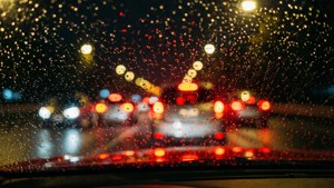 夜間汽車擋風玻璃上的雨滴與模糊的城市燈光