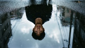 年輕男子倒轉的臉孔映照在城市街道的雨水坑中。