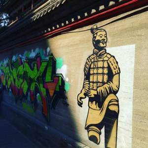 黃色兵馬俑壁畫，旁邊是色彩繽紛的塗鴉，位於傳統屋頂下的城市牆上。