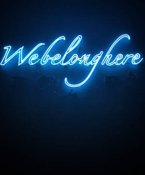 深色牆壁上寫著 We belong here 的藍色霓虹燈牌。