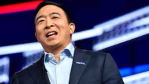 穿西裝的男子在活動中微笑，身後有藍色和紅色的舞台燈光。 — 政治 壁紙