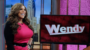 Wendy Williams 在她的脫口秀佈景中微笑，身後是城市景觀。 — 美國 壁紙