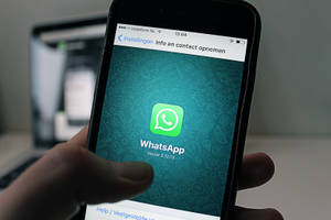 手拿著電話，顯示WhatsApp設定畫面，背景為青綠色。