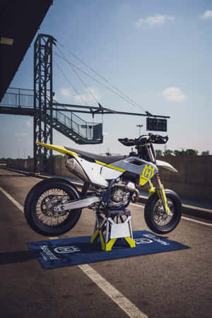 在賽車場展示的白色和黃色 Husqvarna 越野電單車。 — iPhone Duo 壁紙