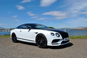 白色 Bentley 跑車停在湖邊，背景有帆船。 — MacBook Air M3 壁紙