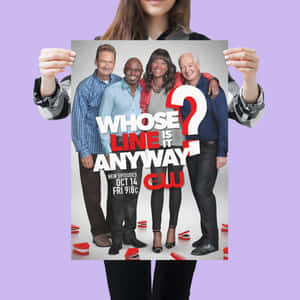 一個人手持《Whose Line Is It Anyway?》電視節目海報，海報上有四位微笑的演員。