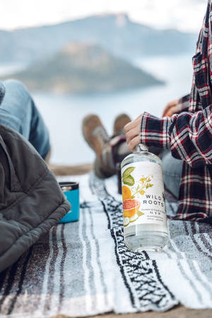 兩人在湖邊放鬆，背景有山，手持氈酒瓶在毯子上
