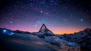 星空暮色下白雪覆蓋的山峰，前景有發光的藍色燈光。 — 冬天桌面 壁紙