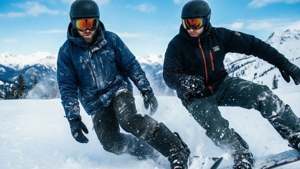 兩個男人在雪山斜坡上滑雪，背後有山脈