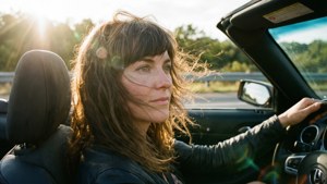 女子在金色日落時分駕駛敞篷車，風吹動頭髮。