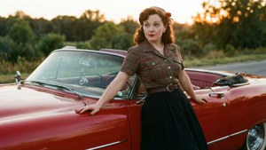 身穿1950年代服裝的女人在日落時靠在紅色經典開篷車上。