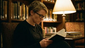 女性在溫暖照明的圖書館中閱讀書籍，背景有書架。
