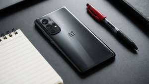 黑色OnePlus手機、紅色筆和橫線筆記本在深灰色桌上