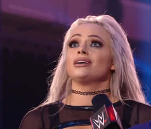 WWE摔角手在紫色燈光下在舞台上對著麥克風說話。
