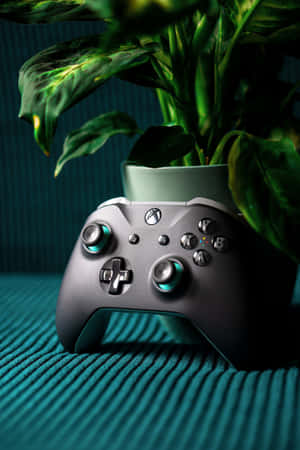 銀色Xbox控制器旁邊有一盆盆栽植物，置於翠綠色紋理表面上。 — Huawei MatePad Air (2025) 壁紙