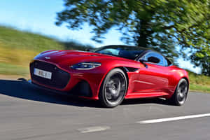 紅色Aston Martin跑車在鄉村道路上飛馳，背景有綠色樹木。 — MacBook Pro 14 壁紙
