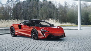 紅色McLaren跑車停放在彎曲的石頭車道上，靠近蘆葦和樹木。