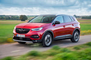 紅色Opel SUV在鄉村道路上穿過綠色田野行駛。 — Surface Pro 壁紙