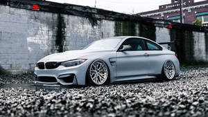 啞光銀色BMW M4雙門跑車停放在碎石上，靠近混凝土牆。