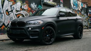 啞光黑色BMW X6 SUV停在城市街道上色彩繽紛的塗鴉牆旁邊。