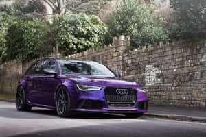 紫色 Audi RS6 Avant 停泊在石牆旁，旁邊有綠色樹木。 — Audi R8 GIF 壁紙