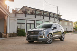 灰色 Cadillac SUV 停泊在設有屋頂露台的現代建築前，夕陽西下。 — Surface Laptop 壁紙