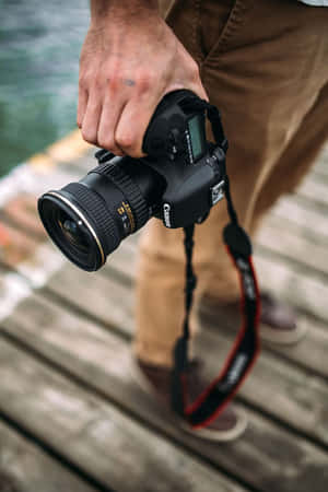 近距離拍攝一隻手喺水邊木碼頭上，手持Canon DSLR相機。 — 小米18 Fold 壁紙