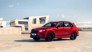 紅色賓利Bentayga SUV停泊在石頭廣場的現代建築附近。 — iMac 壁紙