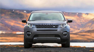灰色 Land Rover Discovery 停泊在湖邊，背景是暮色中的山脈。