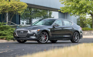深灰色 Genesis G70 轎車停放在現代建築附近，周圍有綠樹。 — Steam Deck OLED 壁紙