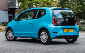 一輛亮藍色的Volkswagen Up! 停在城市街道上，靠近綠樹。 — Steam Deck OLED 壁紙