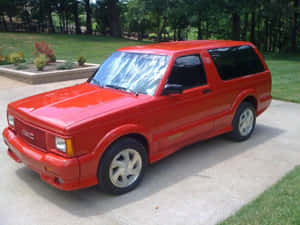 紅色GMC Typhoon SUV停在混凝土車道上，背景有草地和樹木。 — 4:3 壁紙