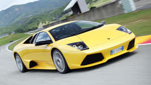 黃色林寶堅尼 Murciélago 在賽道上飛馳，背景是山巒。 — 蘭博基尼 壁紙