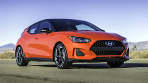 橙色現代Veloster N跑車停在沙漠公路上，遠處有山脈。 — 日落 壁紙