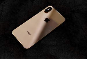 金色iPhone X放在黑色布料上，帶柔和光線和陰影。