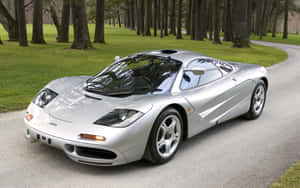 銀色McLaren F1超級跑車停泊在彎曲的道路上，周圍有樹木和草地。 — Steam Deck OLED 壁紙