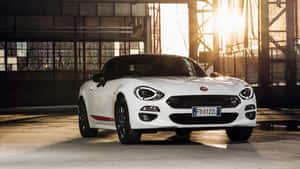 日落時工業倉庫中的白色Fiat 124 Spider開篷車。 — iMac 壁紙